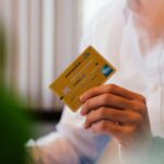 Person holding a credit card, representing everyday grocery and gas purchases