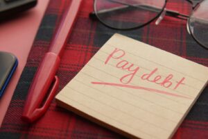 A handwritten note reading pay debt next to a pen and glasses, symbolizing a debt payoff plan